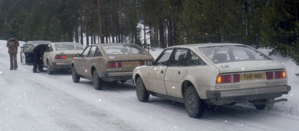 four cars parked in line on snow-covered roadblack camouflaged car with yellow tape simulating a grille